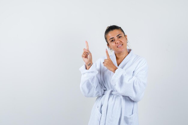 Señorita en bata de baño apuntando hacia arriba y mirando alegre