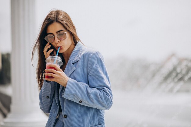 Señorita bebiendo té helado en el parque y hablando por teléfono