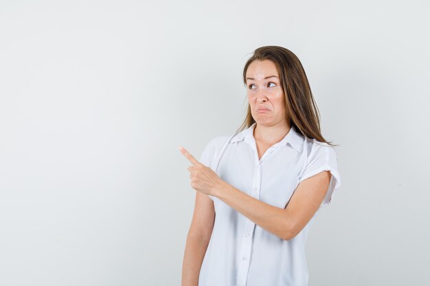 Señorita en blusa blanca apuntando a un lado y mirando molesto