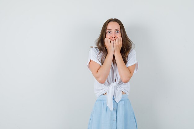 Señorita en blusa blanca, falda azul tomados de la mano en la boca con los ojos muy abiertos y mirando asustado