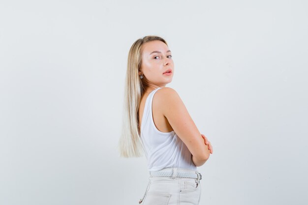 Señorita en blusa blanca manteniendo los brazos cruzados mientras mira a un lado y se ve impresionante.