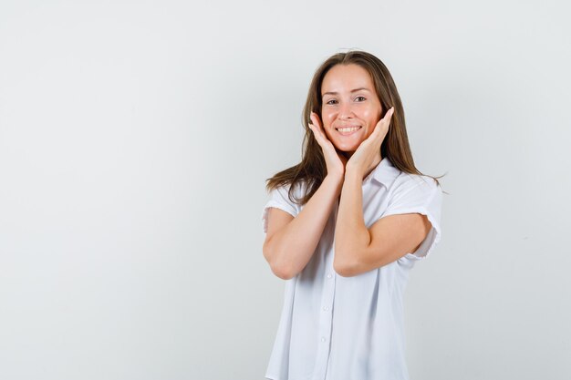 Señorita en blusa blanca tomados de la mano en el rostro y mirando contento