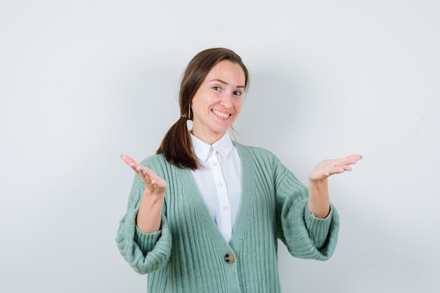 Señorita en blusa, cardigan abriendo los brazos para un abrazo y mirando alegre, vista frontal.