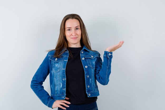 Señorita en blusa, chaqueta fingiendo sostener algo y mirando confiada, vista frontal.