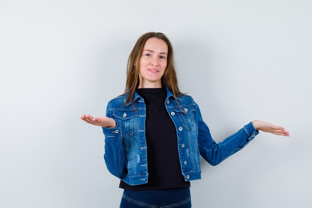 Señorita en blusa, chaqueta presentando o comparando algo y mirando confiado, vista frontal.