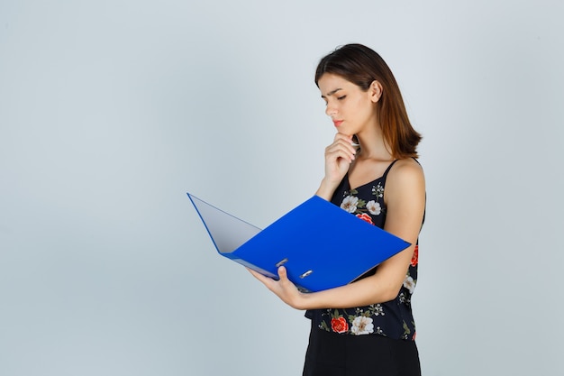 Señorita en blusa, falda mirando documentos en carpeta y mirando pensativo, vista frontal.