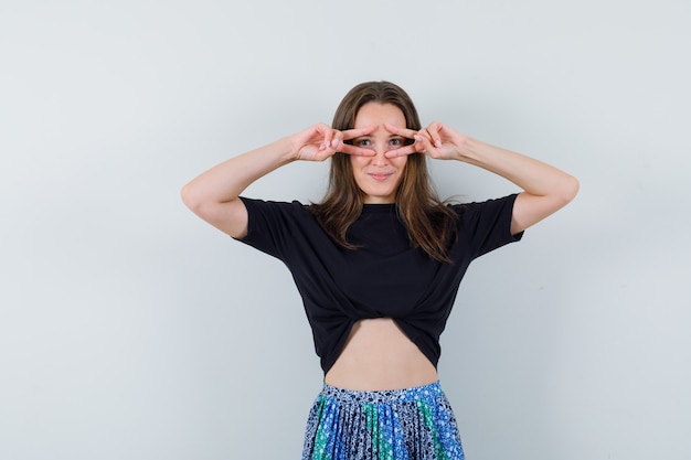 Señorita en blusa, falda mostrando el signo V en los ojos y luciendo bonita