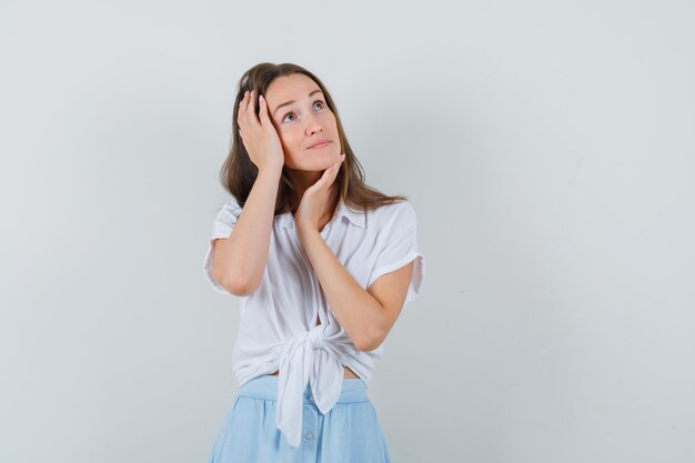 Señorita en blusa, falda tomados de la mano en la cara y la cabeza y luciendo sensato