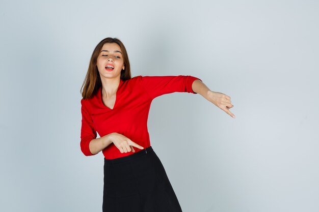 Señorita en blusa roja, falda apuntando hacia abajo y mirando feliz