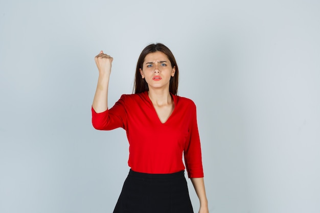 Señorita de blusa roja, falda levantando puño cerrado y mirando rencoroso