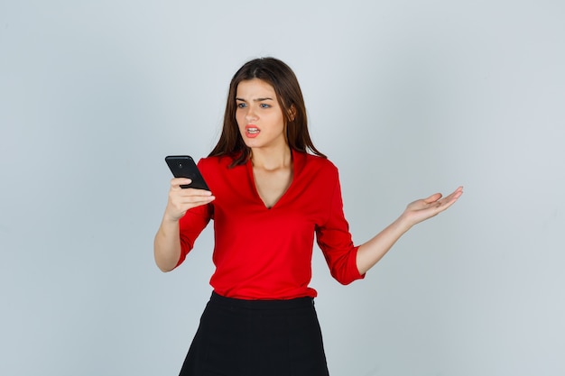 Señorita en blusa roja, falda mirando teléfono móvil