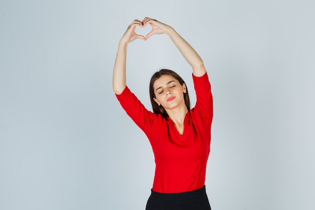 Señorita en blusa roja, falda mostrando gesto de corazón y luciendo bonita