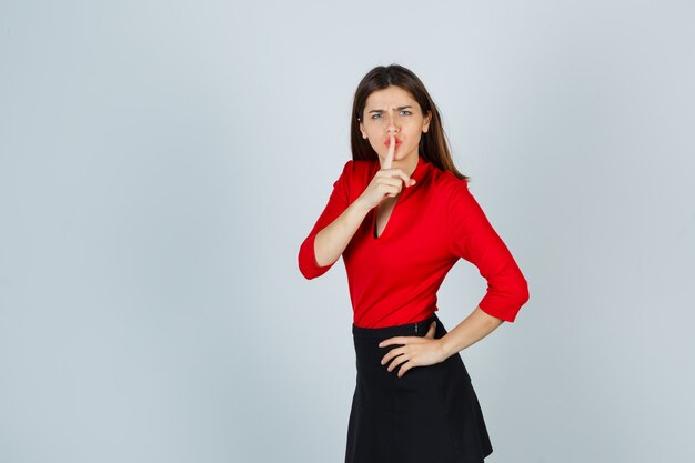 Señorita en blusa roja, falda negra mostrando gesto de silencio