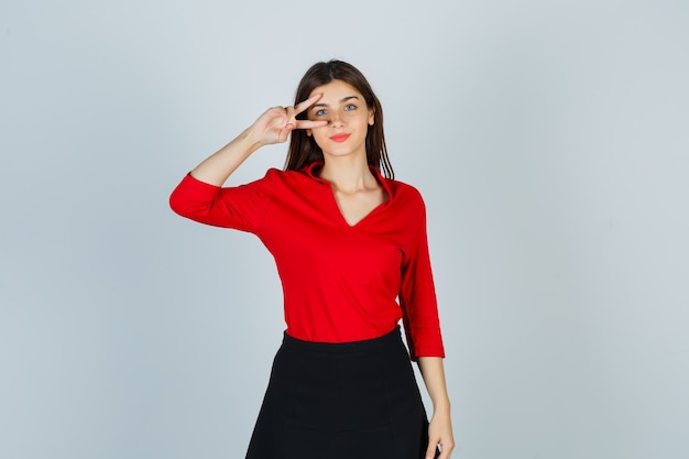 Señorita en blusa roja, falda negra que muestra el signo v en el ojo y parece confiada