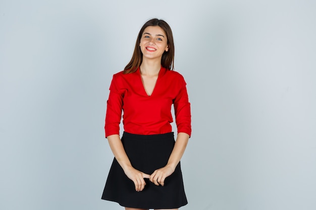 Foto gratuita señorita en blusa roja, falda posando mientras mira a cámara y mirando alegre