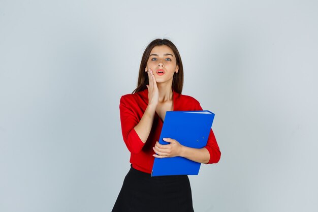 Señorita en blusa roja, falda sosteniendo la carpeta mientras mantiene la mano