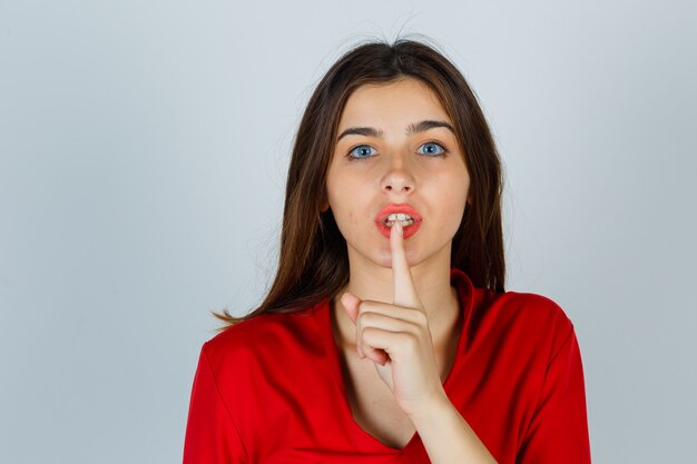 Señorita en blusa roja mostrando gesto de silencio y mirando serio