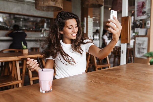 Señorita en café con muebles de madera hace selfie