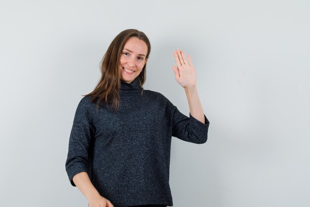 Señorita en camisa agitando la mano para saludar y mirar alegre