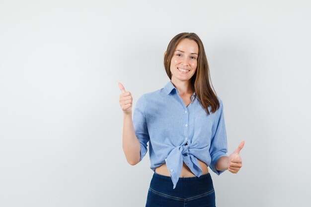 Señorita en camisa azul, pantalones mostrando los pulgares hacia arriba y mirando complacido