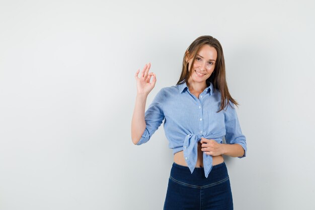 Señorita en camisa azul, pantalones mostrando signo ok y mirando feliz