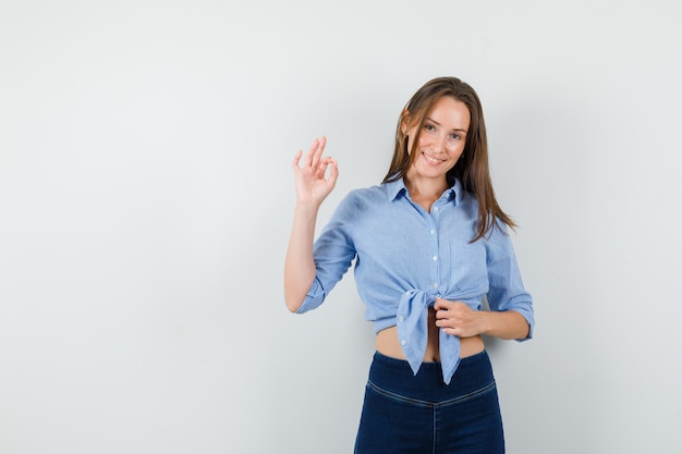 Señorita en camisa azul, pantalones mostrando signo ok y mirando feliz