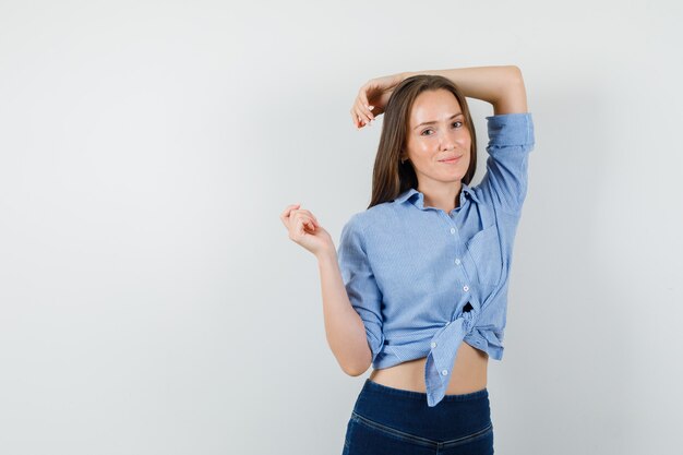 Señorita en camisa azul, pantalones posando mientras está de pie y mirando seductor