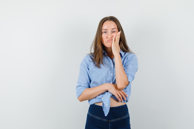 Señorita en camisa azul, pantalones sosteniendo la palma en la mejilla y mirando agotado