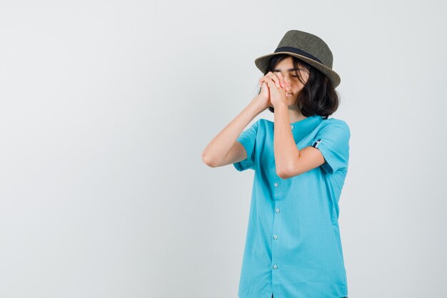 Señorita con camisa azul, sombrero combinando manos para rezar y lucir esperanzado