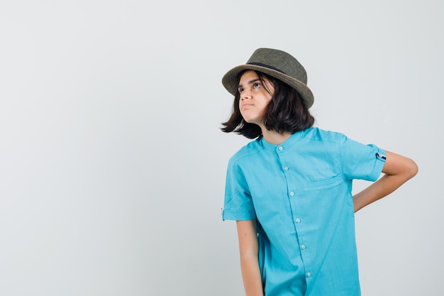 Foto gratuita señorita con camisa azul, sombrero sosteniendo la mano sobre su columna vertebral y mirando preocupado