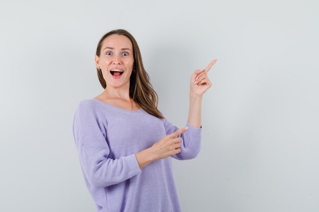 Señorita en camisa casual apuntando a la esquina superior derecha y mirando feliz