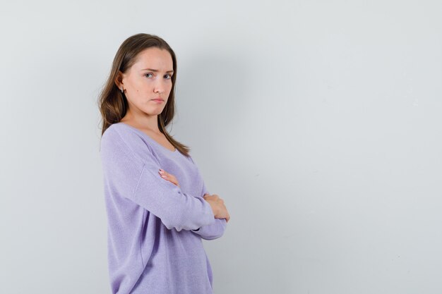 Señorita en camisa casual de pie con los brazos cruzados y mirando triste