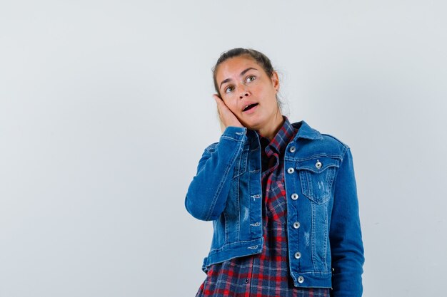 Señorita en camisa, chaqueta apoyando la mejilla en la palma y mirando soñadora, vista frontal.