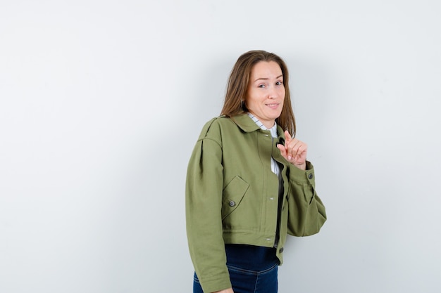 Señorita en camisa, chaqueta apuntando a la cámara y mirando feliz, vista frontal.