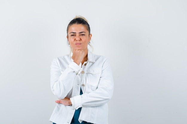 Foto gratuita señorita en camisa, chaqueta blanca apoyando la barbilla en el puño y mirando segura de sí misma, vista frontal.