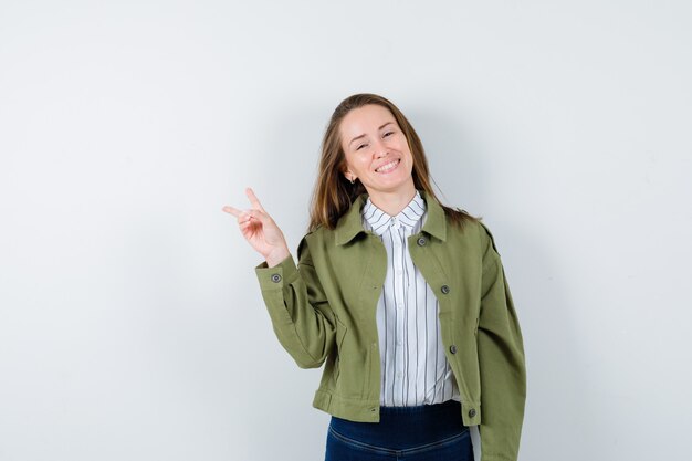 Señorita en camisa, chaqueta mostrando gesto de victoria y mirando alegre, vista frontal.