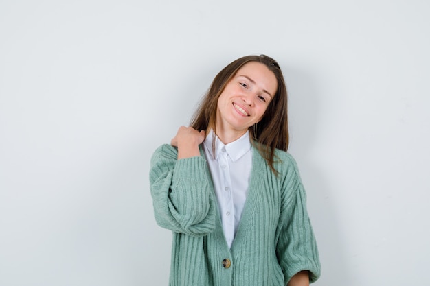 Señorita en camisa, chaqueta de punto con la mano en el hombro y mirando complacido, vista frontal.