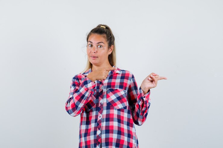 Foto gratuito señorita en camisa a cuadros apuntando hacia el lado derecho y mirando alegre, vista frontal.
