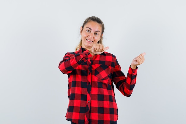 Señorita en camisa a cuadros apuntando a un lado con los pulgares y mirando alegre