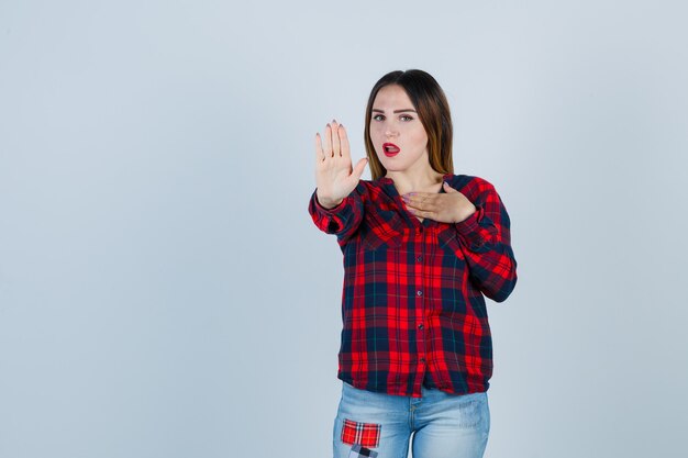 Señorita en camisa a cuadros, jeans sin gesto y mirando sorprendido, vista frontal.