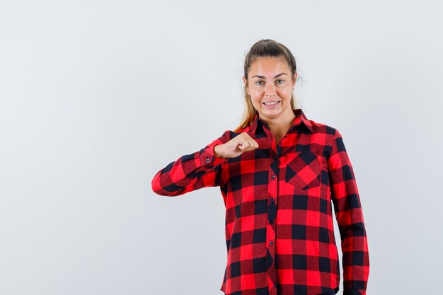 Señorita en camisa a cuadros manteniendo el puño cerrado y mirando confiado