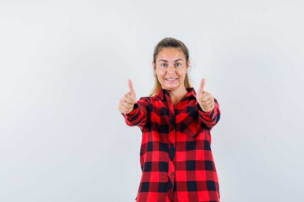 Señorita en camisa a cuadros mostrando doble pulgar hacia arriba y mirando alegre