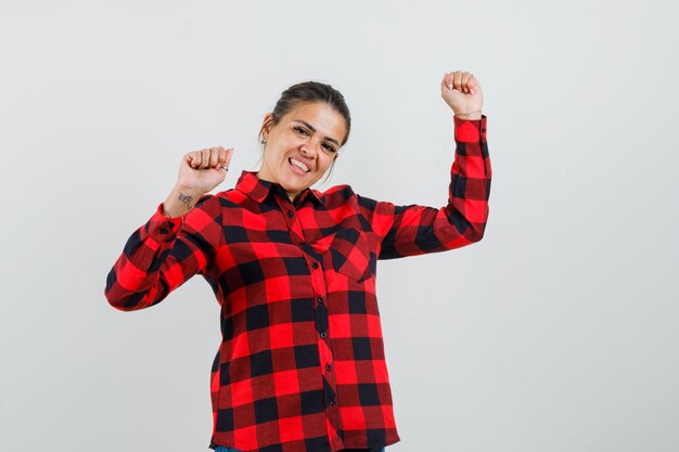 Señorita en camisa a cuadros que muestra el gesto del ganador y se ve feliz