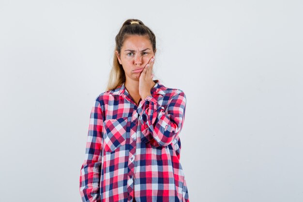 Señorita en camisa a cuadros que sufre de dolor de muelas y se ve incómoda, vista frontal.