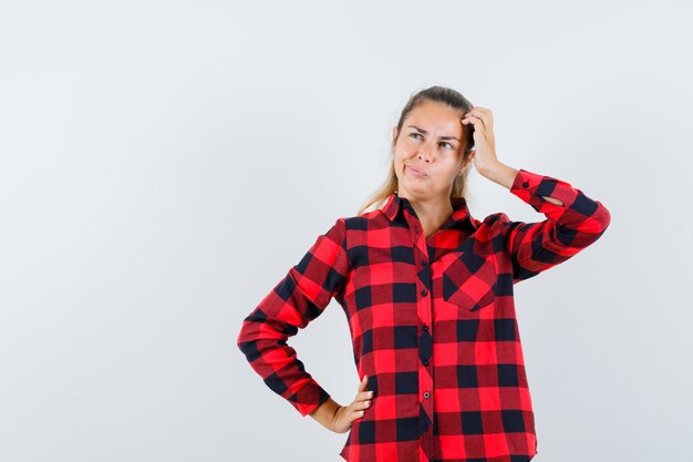 Señorita en camisa de cuadros rascándose la cabeza y mirando vacilante