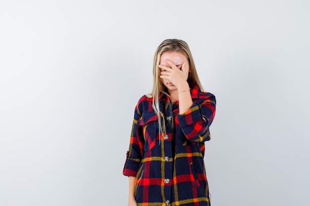 Señorita en camisa a cuadros sosteniendo la mano en la cara y con aspecto cansado, vista frontal.