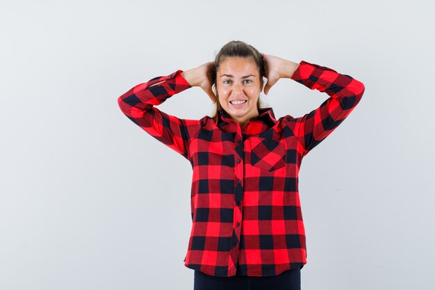 Señorita en camisa a cuadros tomados de la mano detrás de la cabeza y mirando feliz