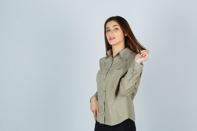 Señorita en camisa, falda jugando con su cabello y mirando confiada, vista frontal.