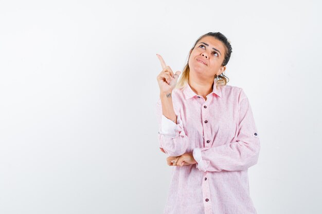 Señorita en camisa rosa apuntando hacia arriba y mirando alegre