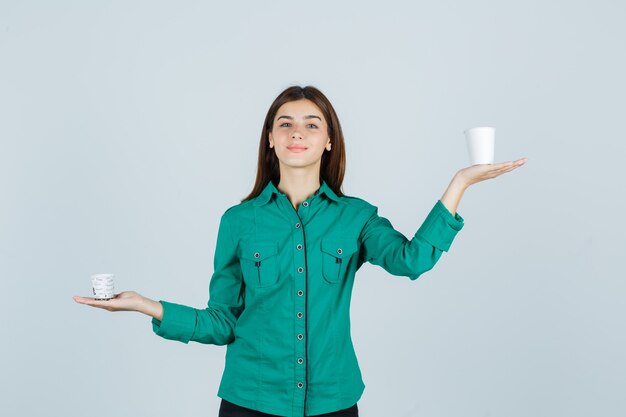 Señorita en camisa sosteniendo vasos de plástico de café y mirando complacido, vista frontal.
